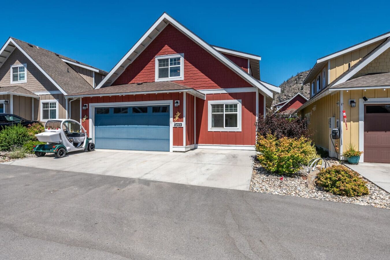 A residential house with a red exterior, a garage, and a small green vehicle parked in the driveway.