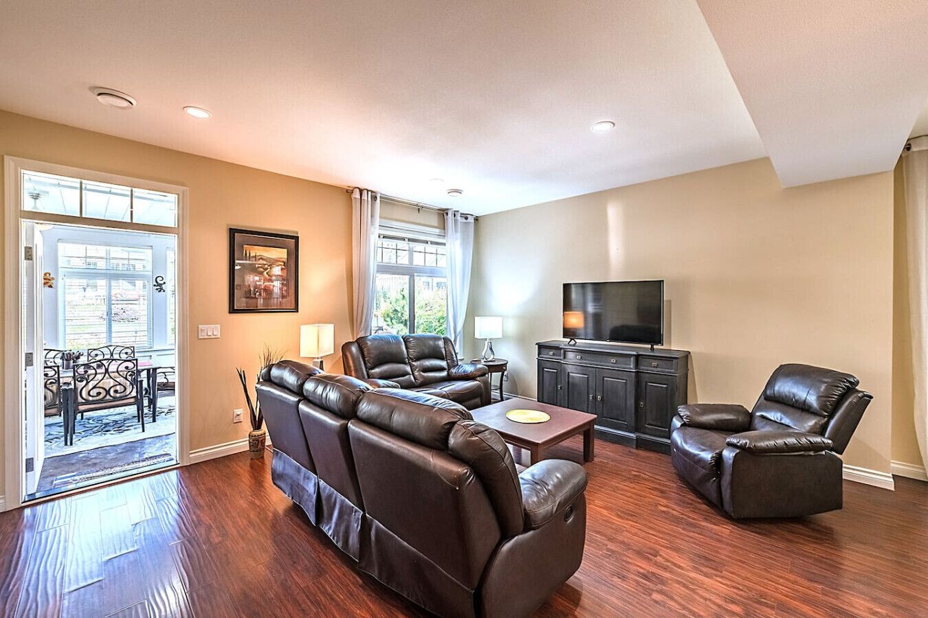 A living room with a sectional sofa, a recliner, a coffee table, a TV on a cabinet, and a balcony with outdoor furniture.