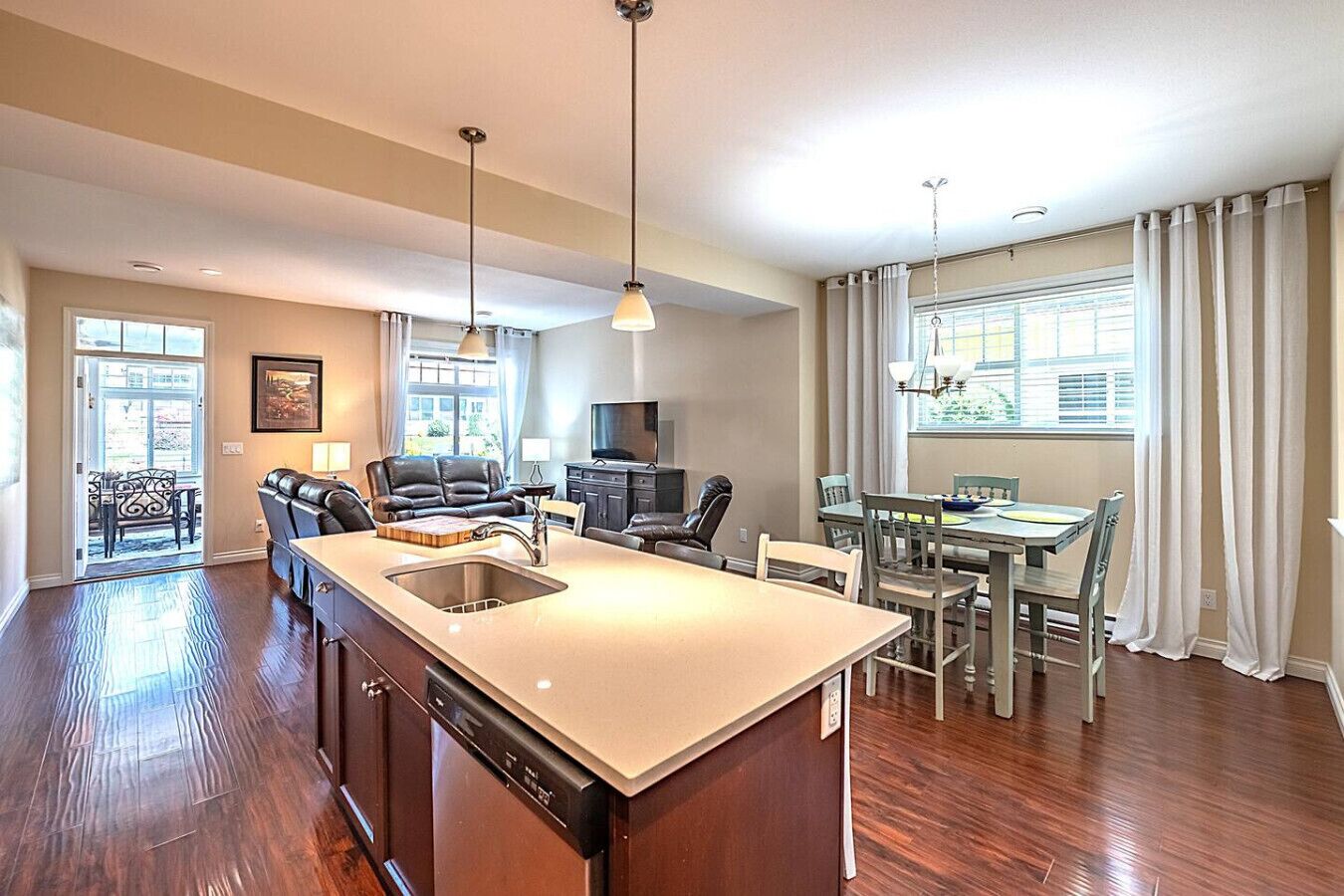 A modern kitchen with a central island, dining area with chairs, a sofa, and a TV.