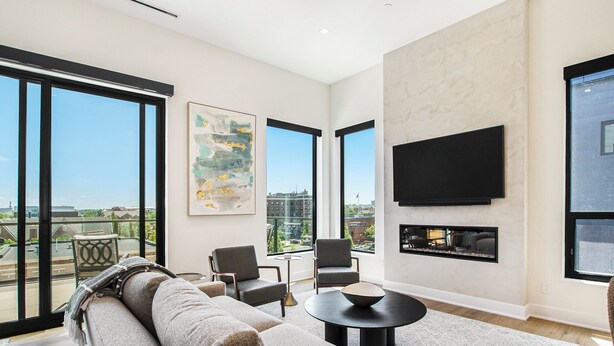 A modern living room with a sofa, chairs, a coffee table, and a fireplace. Large windows offer a city view.