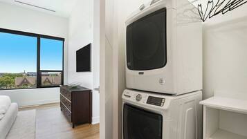 A modern room with a large window, a stacked washer and dryer, a dark wooden dresser, and a white sofa.