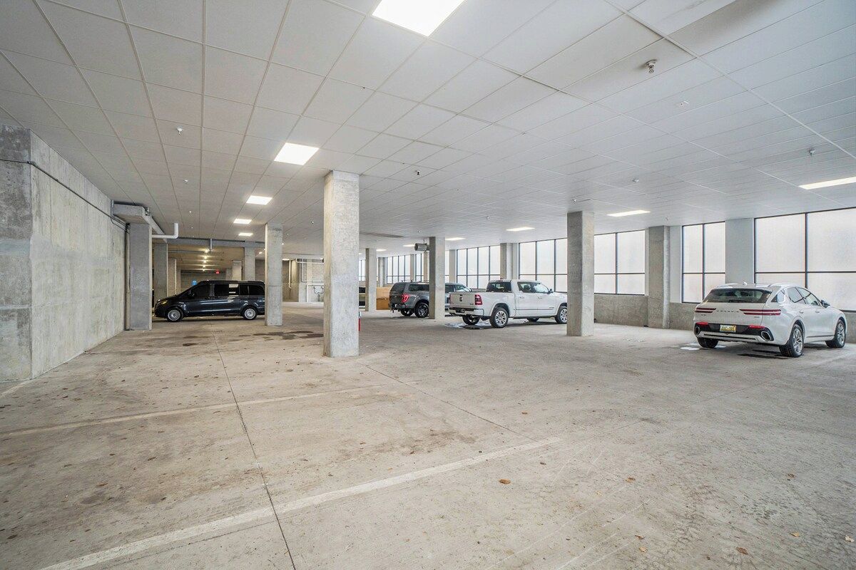 A parking garage with concrete pillars, a few parked cars, and a clear ceiling with lights.