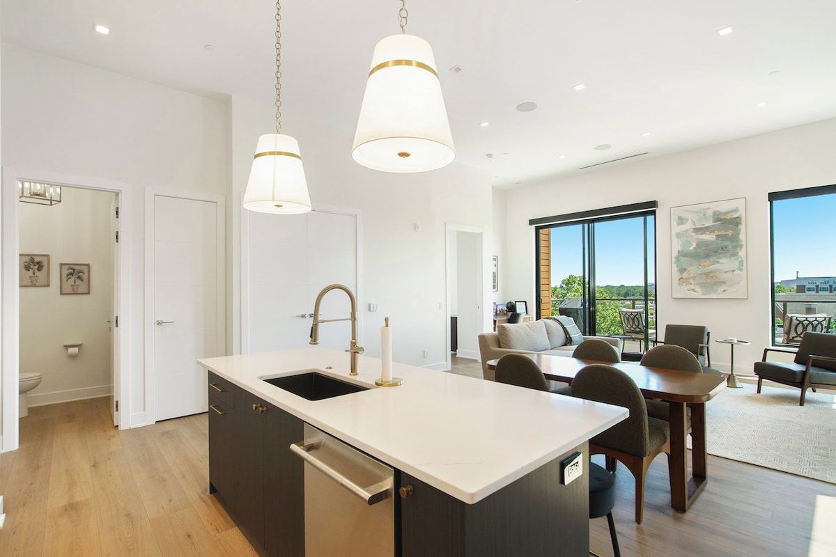A modern kitchen with a central island, pendant lighting, and a view to the living area.