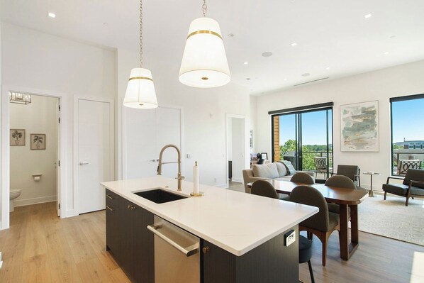 Una cocina moderna con una isla central, iluminación colgante y vistas al área de estar.