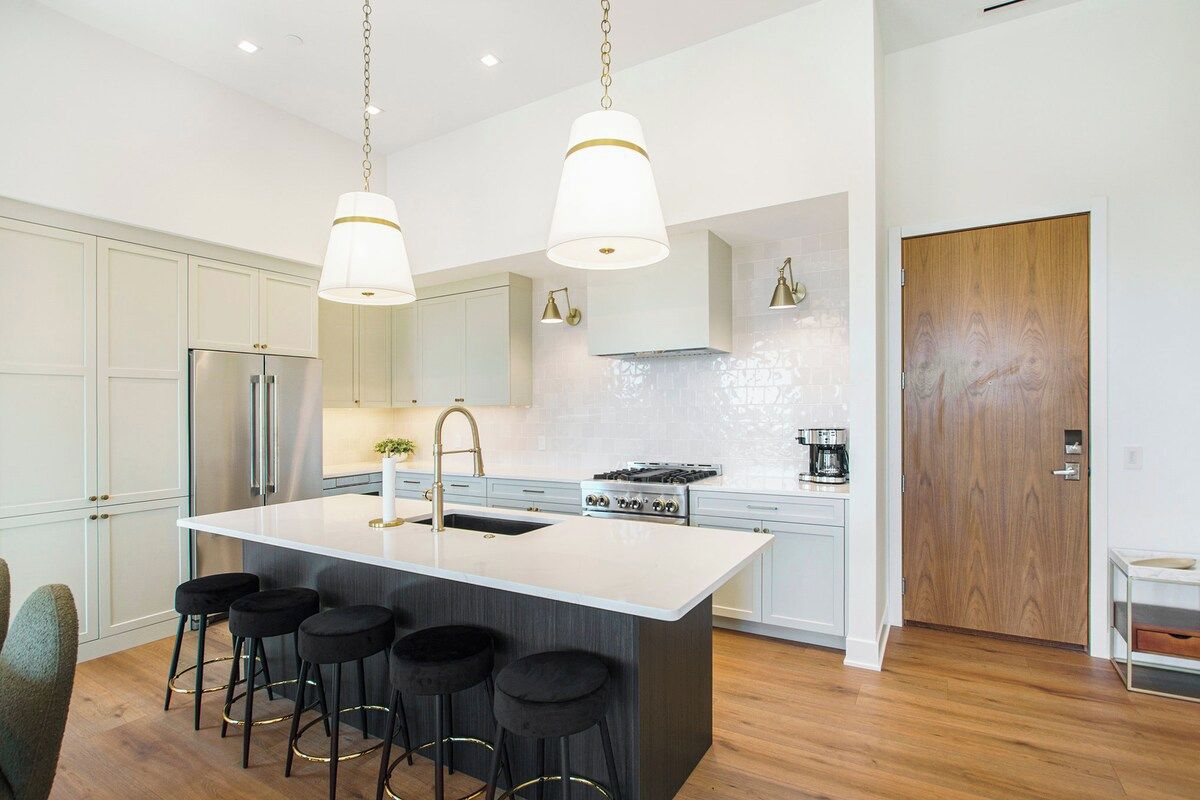 A modern kitchen with a central island, bar stools, stainless steel appliances, and pendant lighting.