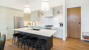 A modern kitchen with a central island, bar stools, stainless steel appliances, and pendant lighting.