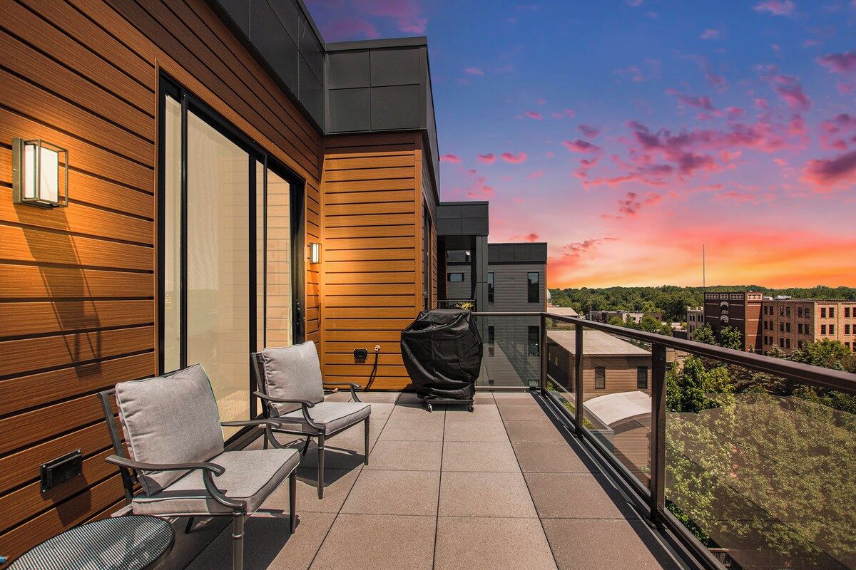 Un balcón con mobiliario exterior, una parrilla y vistas a la ciudad al atardecer.