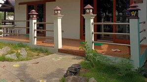 Un edificio pequeño con techo de tejas rojas, paredes blancas y una puerta de madera. Hay dos lámparas tipo farol en el porche.