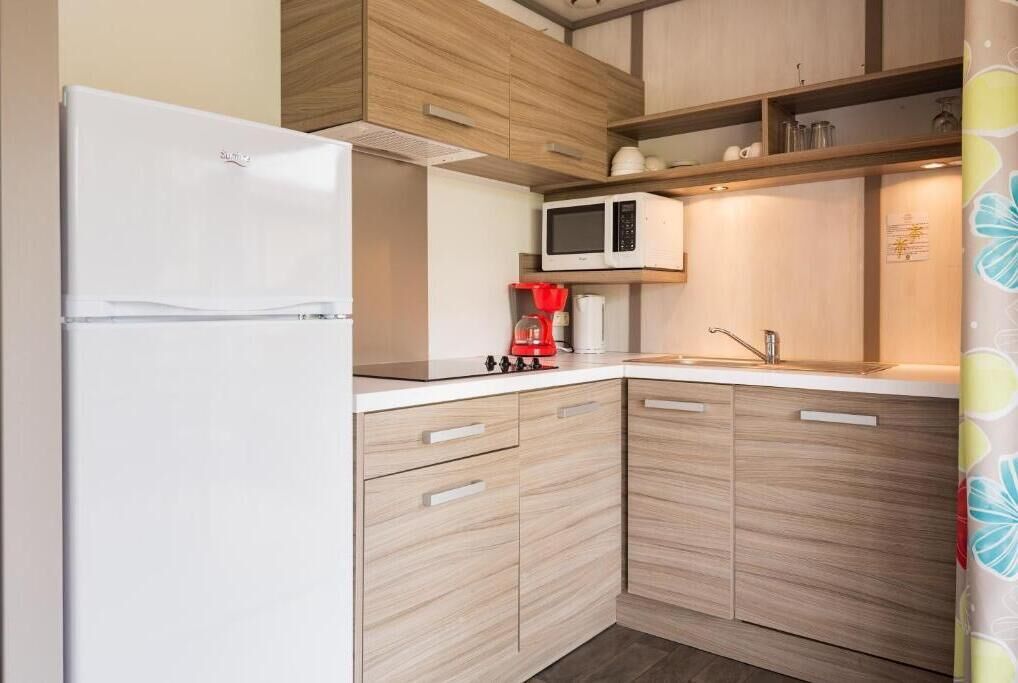 Une cuisine compacte avec un réfrigérateur blanc, un four à micro-ondes et une machine à café posés sur le plan de travail.