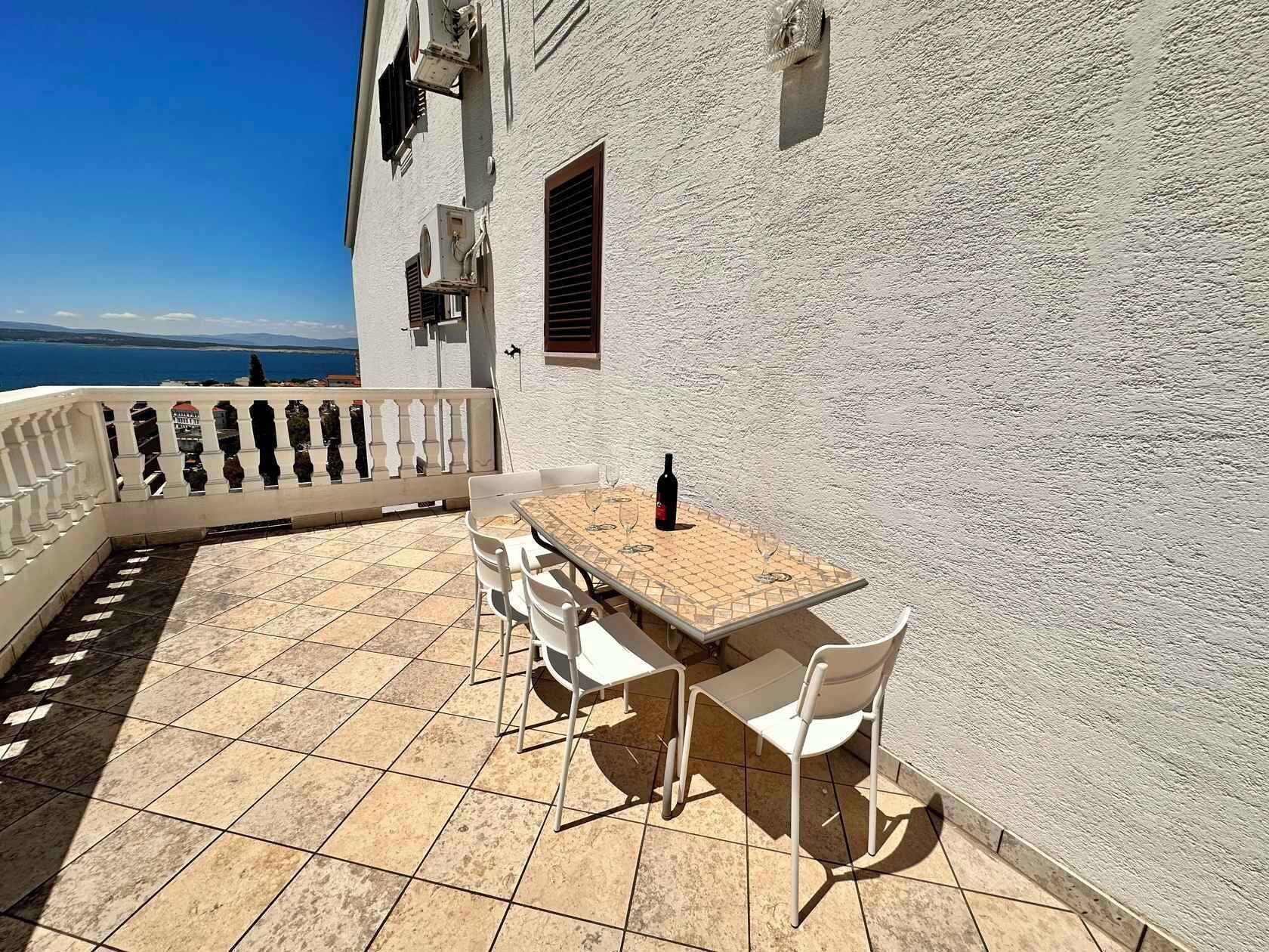 A terrace with a table and chairs, a bottle of wine, and a view of the sea.