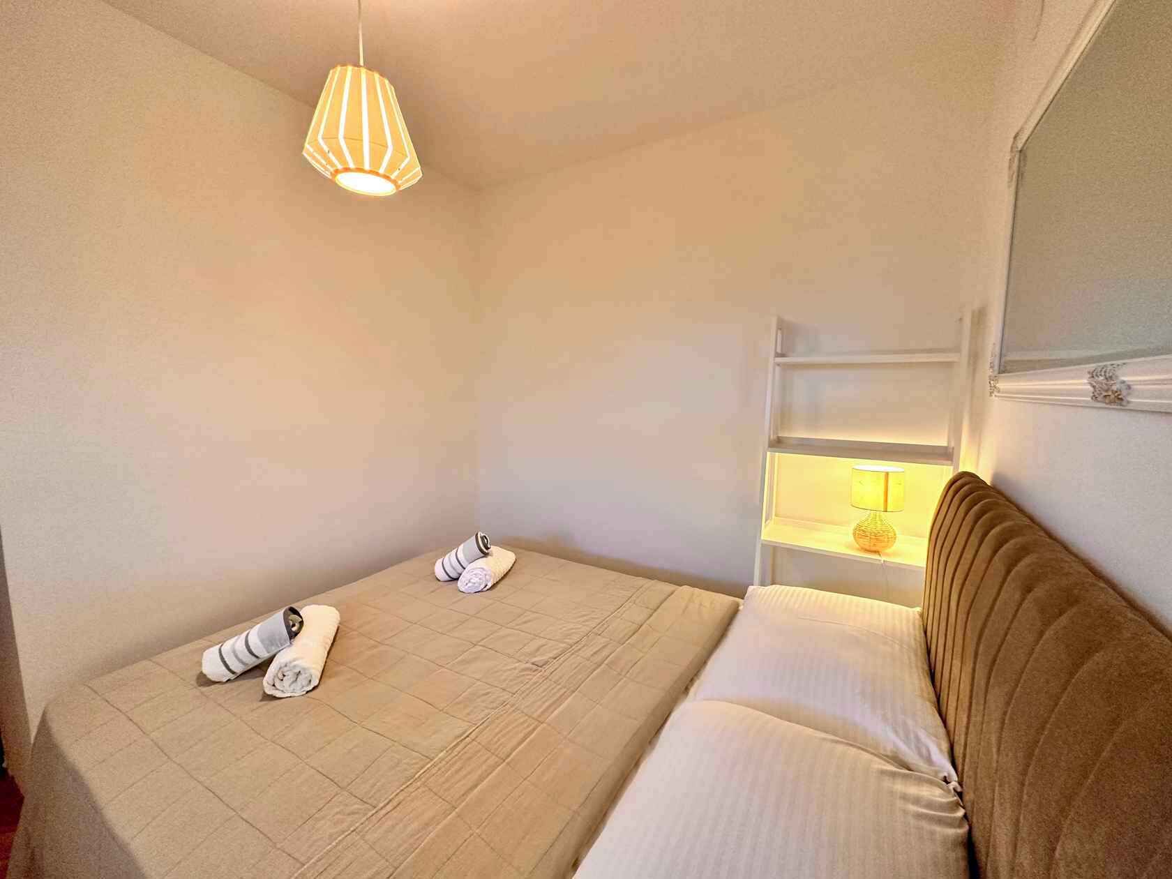 Un dormitorio pequeño y ordenado con cama, lámpara de noche y lámpara colgante.