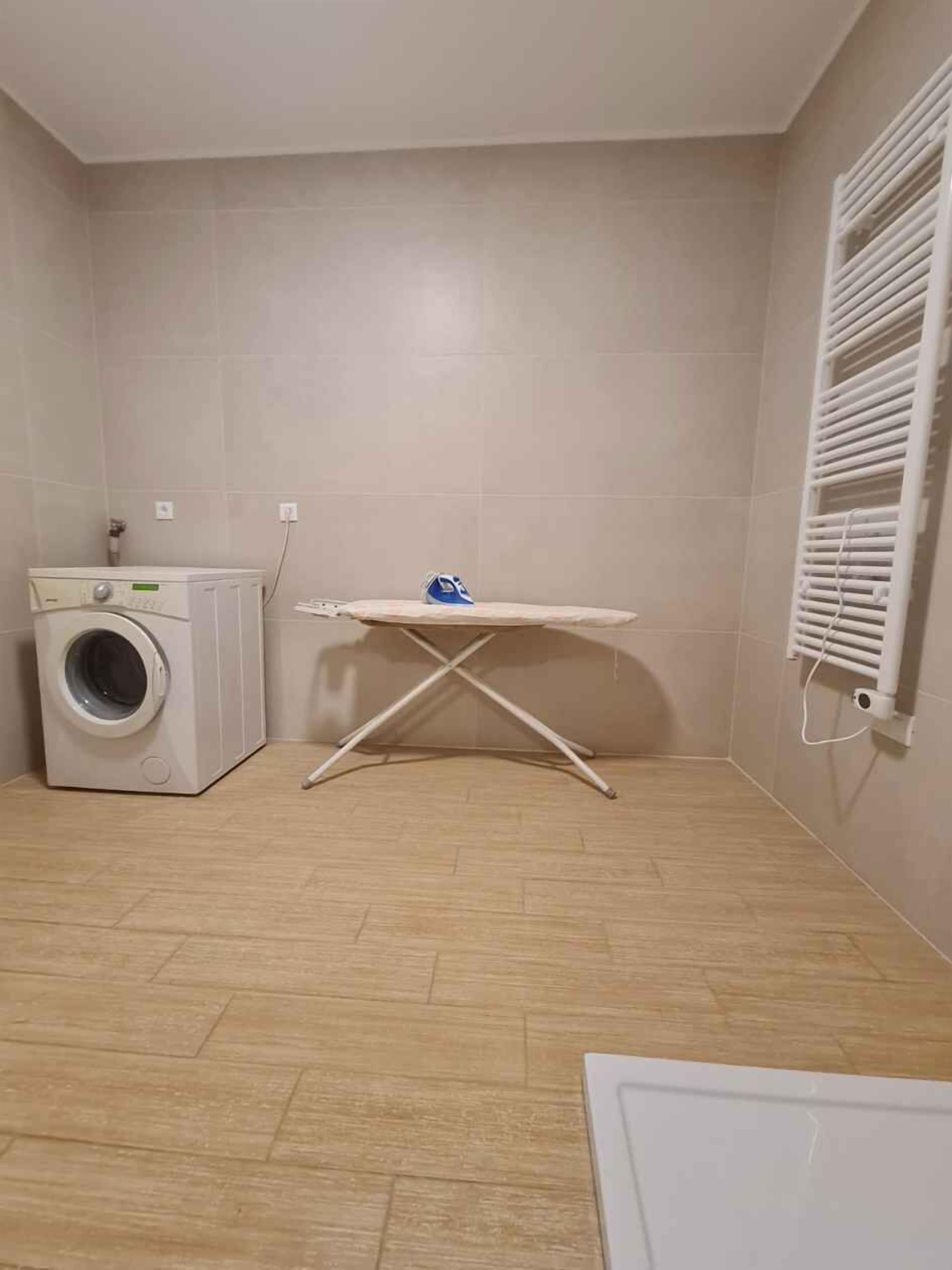 A laundry room with a washing machine, ironing board, and a radiator.