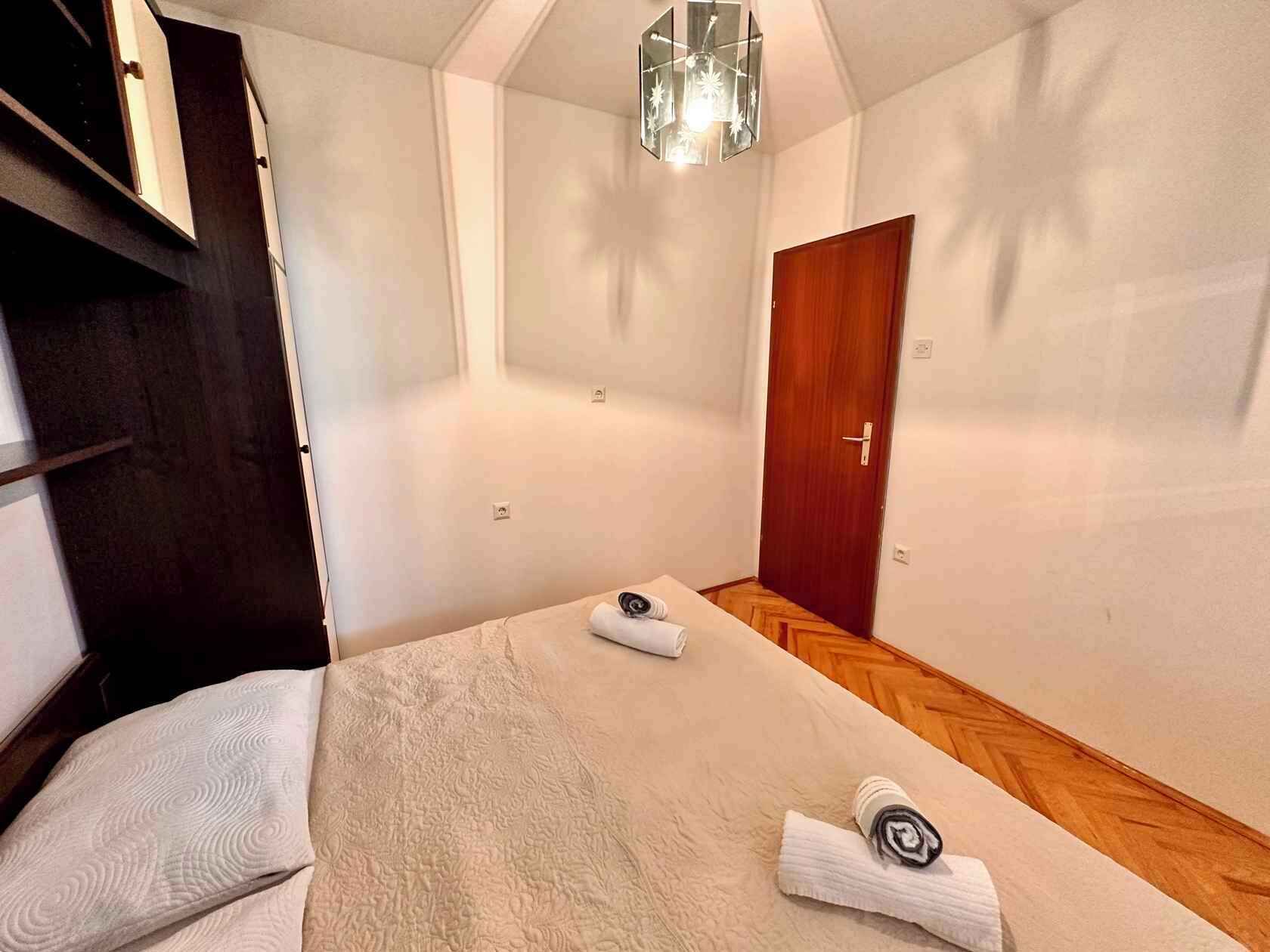 A bedroom with a bed, a wooden door, a small table with a towel, and a hanging light fixture.