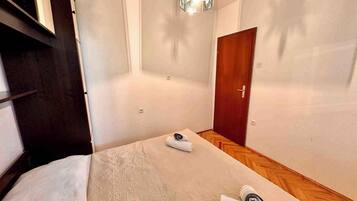 A bedroom with a bed, a wooden door, a small table with a towel, and a hanging light fixture.