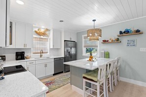 A modern kitchen with white cabinetry, stainless steel appliances, and a central island with seating.