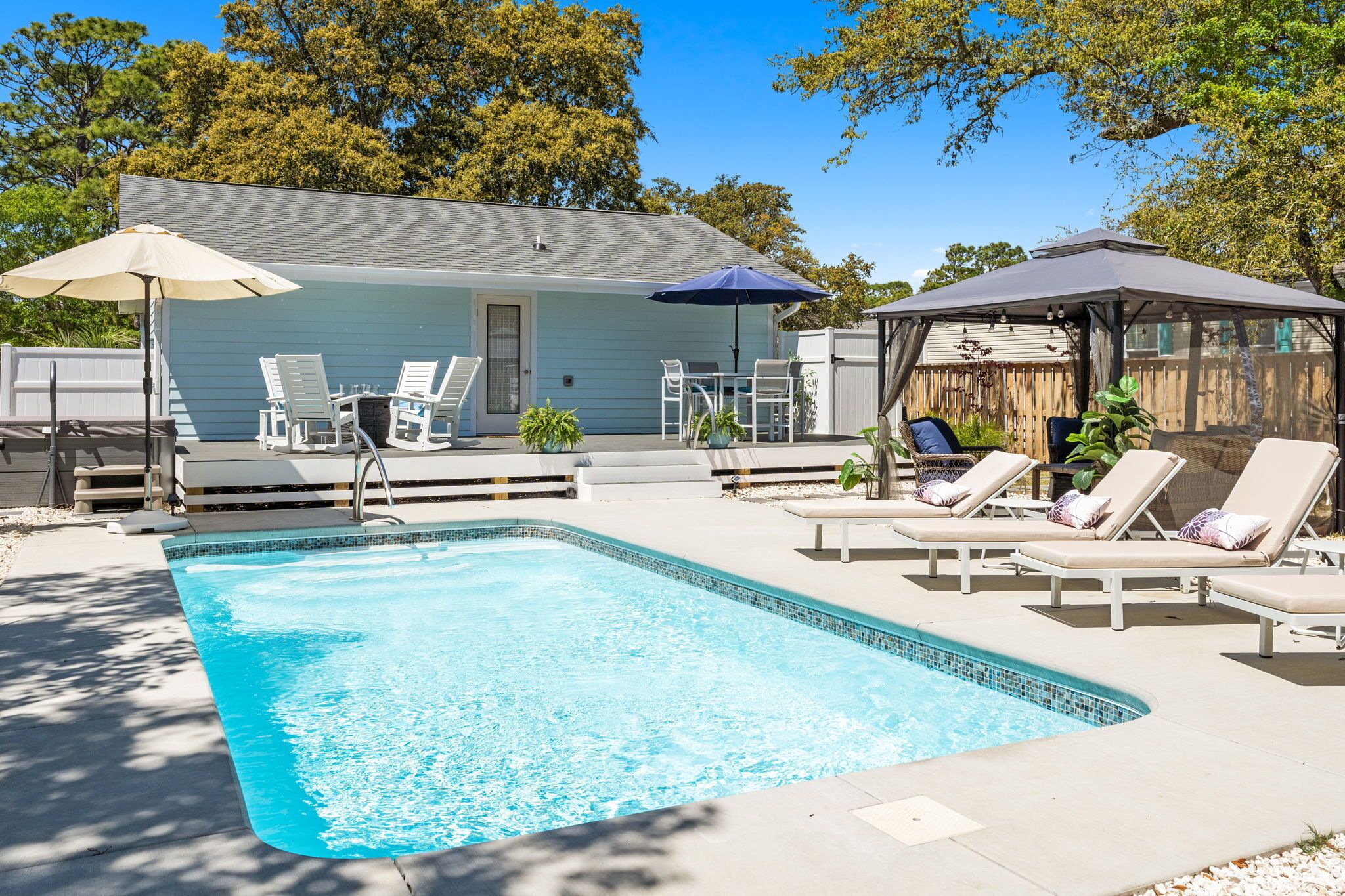 Ein Swimmingpool mit Liegestühlen und Sonnenschirmen, ein überdachter Sitzbereich und ein Haus im Hintergrund.