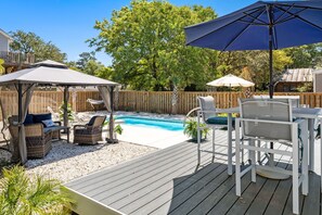 A backyard with a pool, outdoor furniture, and a wooden deck.