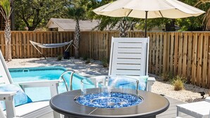 Ein Garten mit Pool, Whirlpool und einer Holzterrasse mit weißen Stühlen und einem Sonnenschirm.