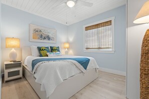 A bedroom with a bed, bedside lamps, a window with blinds, a ceiling fan, and a wall-mounted artwork.