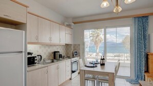 Une cuisine moderne avec un coin repas, de grandes fenêtres offrant une vue sur la mer et un balcon avec une table préparée pour deux personnes.