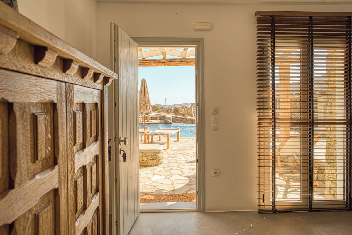 An open door leading to a patio with stone flooring, a pool, and outdoor furniture.