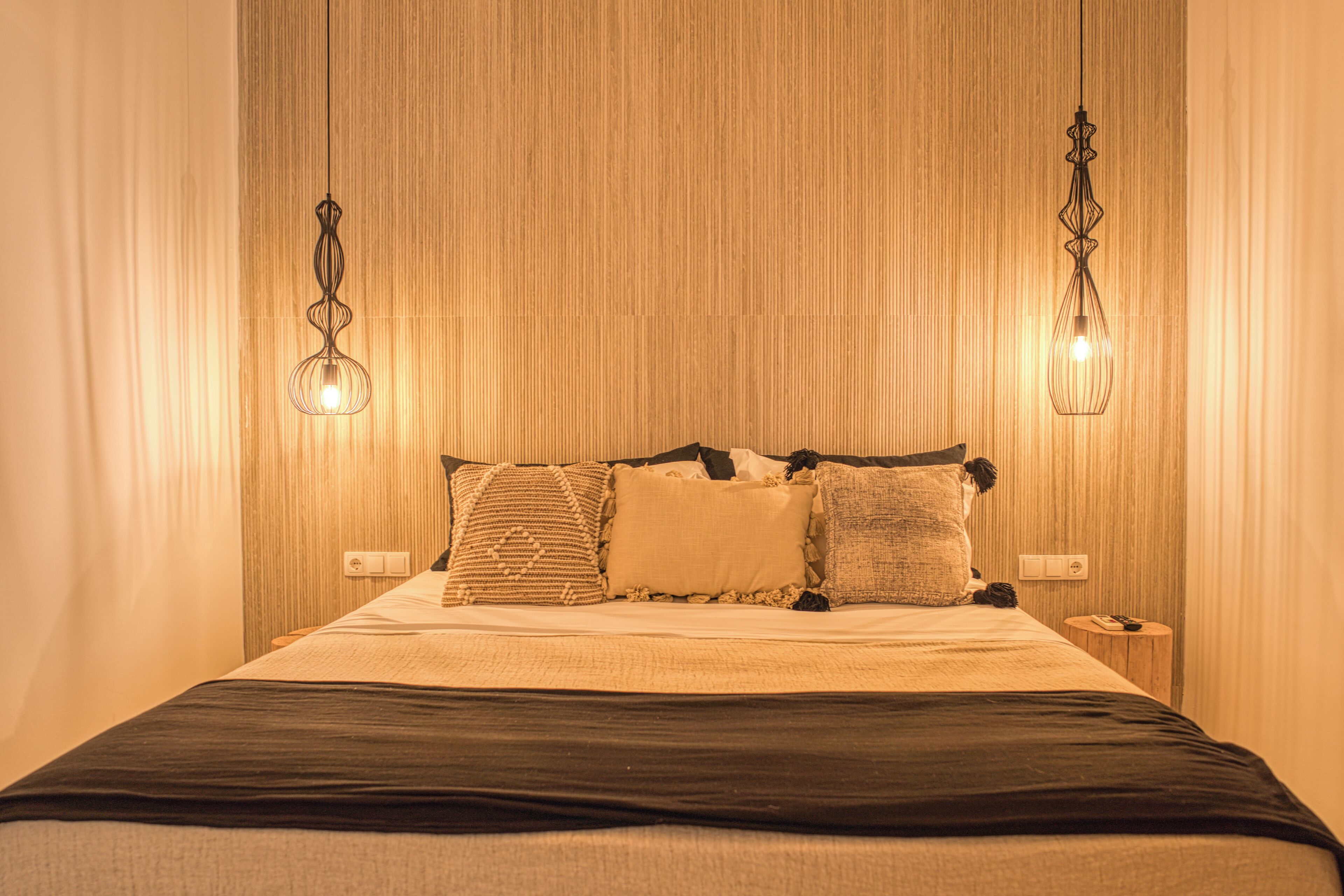 A neatly made bed with a dark bedspread, multiple pillows, and two hanging light fixtures.