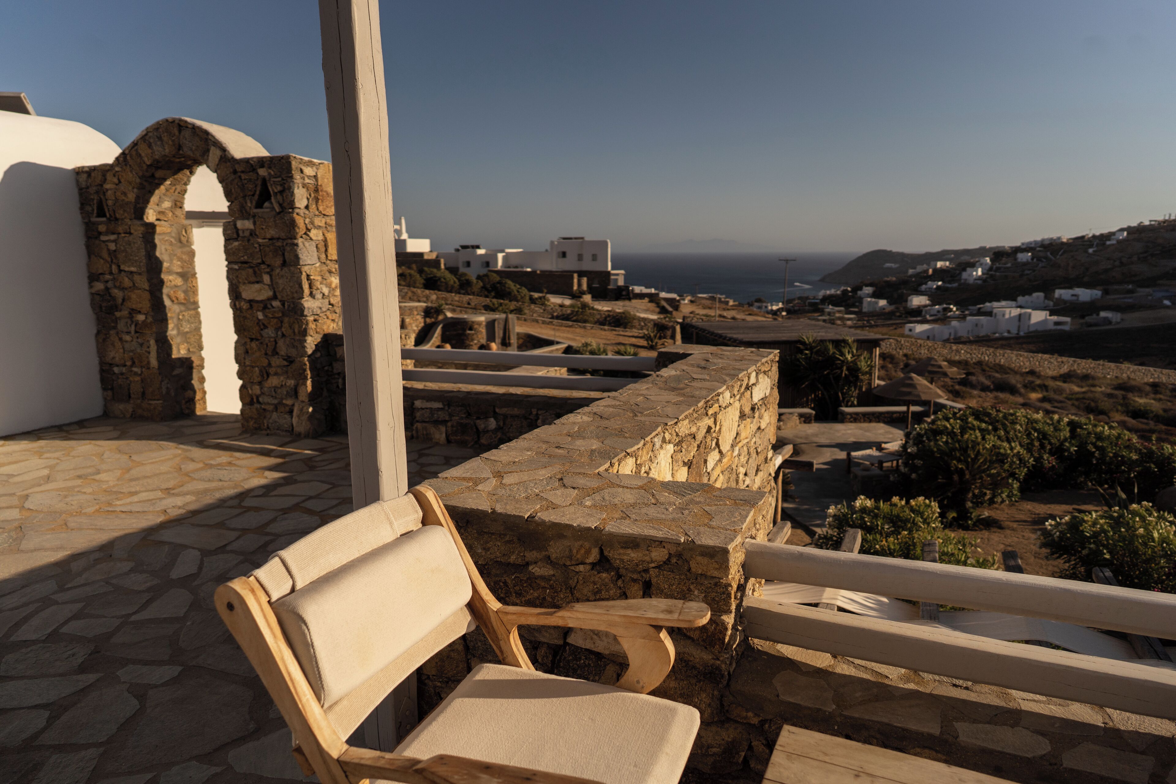 Un banco de piedra en una terraza con vistas a un pueblo costero de edificios blancos y una vista despejada del mar.