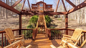 A wooden deck with chairs leading to a wooden staircase and a cabin in the background.