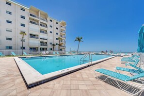 A swimming pool with lounge chairs, a building with balconies, and a clear sky. - Leonardo Arms 106 Beachfront 2B/2B Vacation Condo! Palm Trees And Sunshine! (Fort Myers Beach)