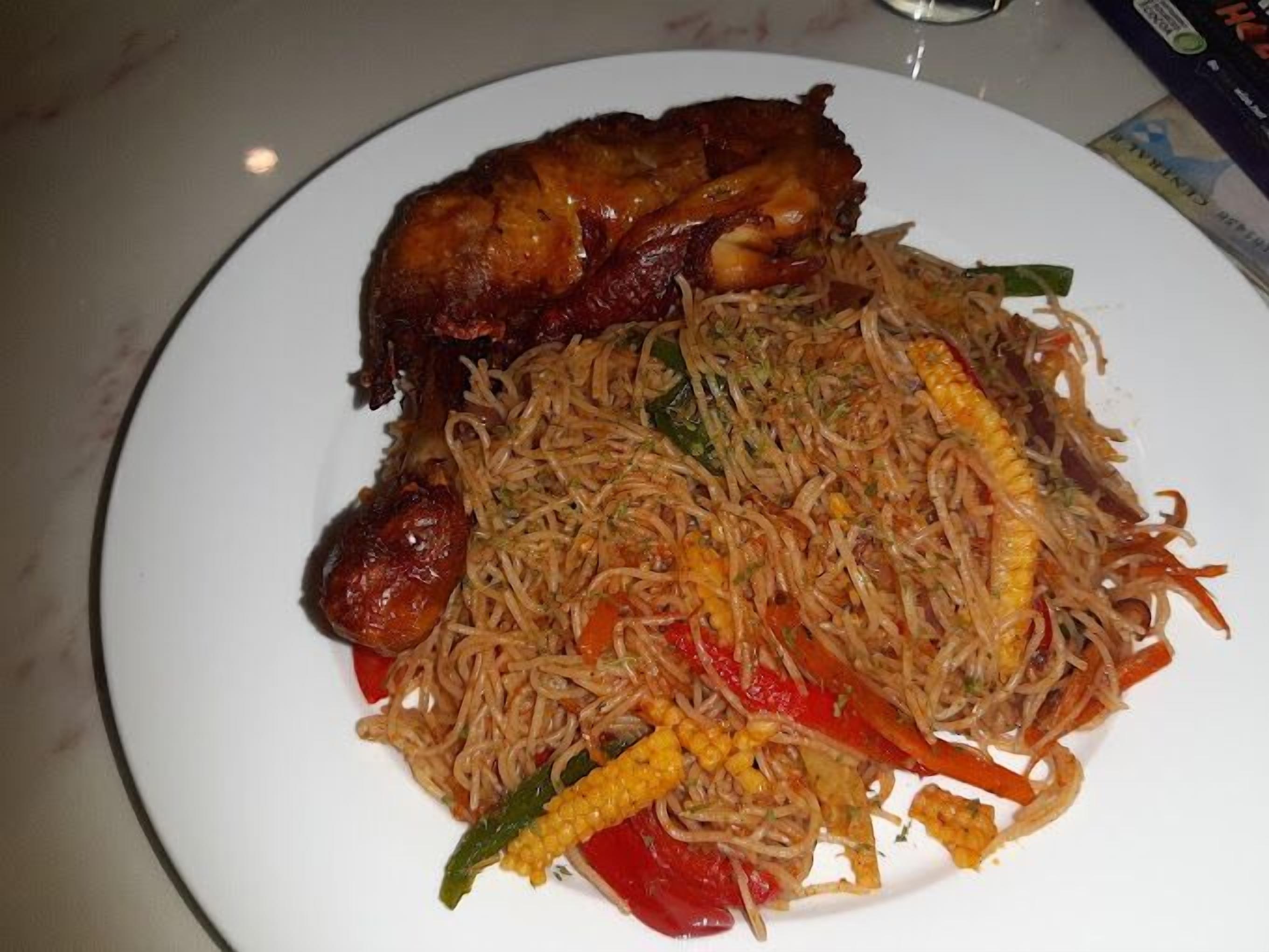 A plate of stir-fried noodles with vegetables and a piece of meat.