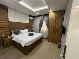 Un dormitorio moderno con una cama grande, cabecera de madera, una mesita de noche, un armario y una lámpara en el techo.