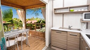 Eine kompakte Küche mit Holzbalkendecke, ein Essbereich mit Metallstühlen und Blick auf Grünflächen.