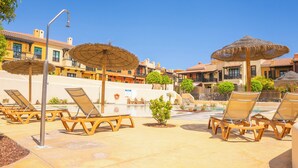A resort pool area with lounge chairs and umbrellas, surrounded by buildings with Mediterranean architecture. - Villa Luisa: Relax with ocean view and swimming pool (Los Abrigos)