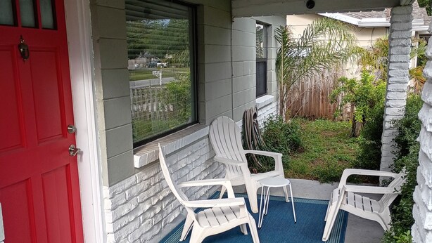 A covered porch with a red door, white chairs, and a small pool.