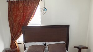 A bed with a headboard, two pillows, a bedside table, and a hanging spider decoration.