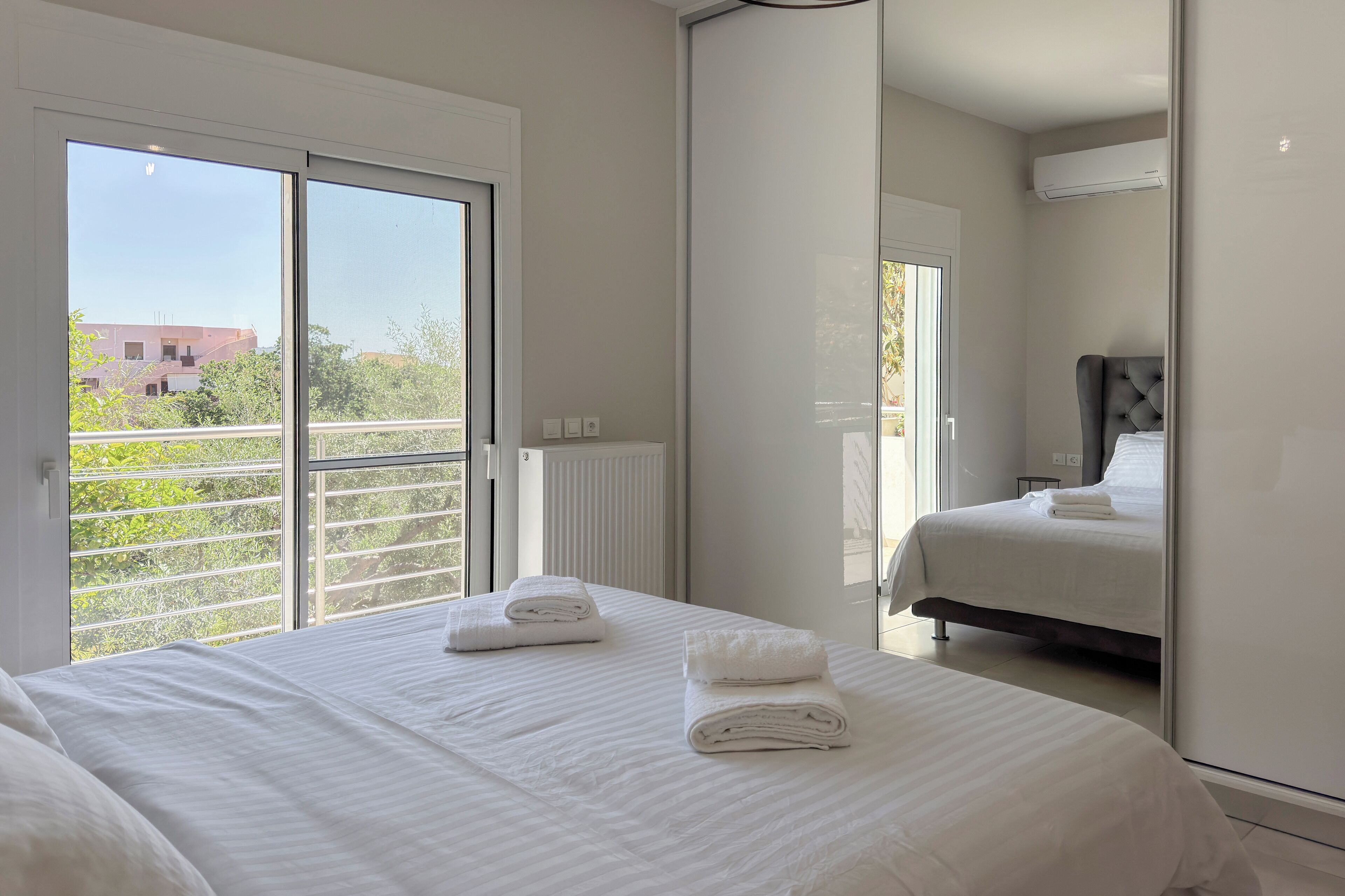 A hotel room with two beds, a large window, and a view of greenery and buildings outside.