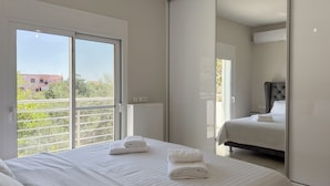 Habitación de hotel con dos camas, un ventanal grande y vistas a zonas verdes y edificios.