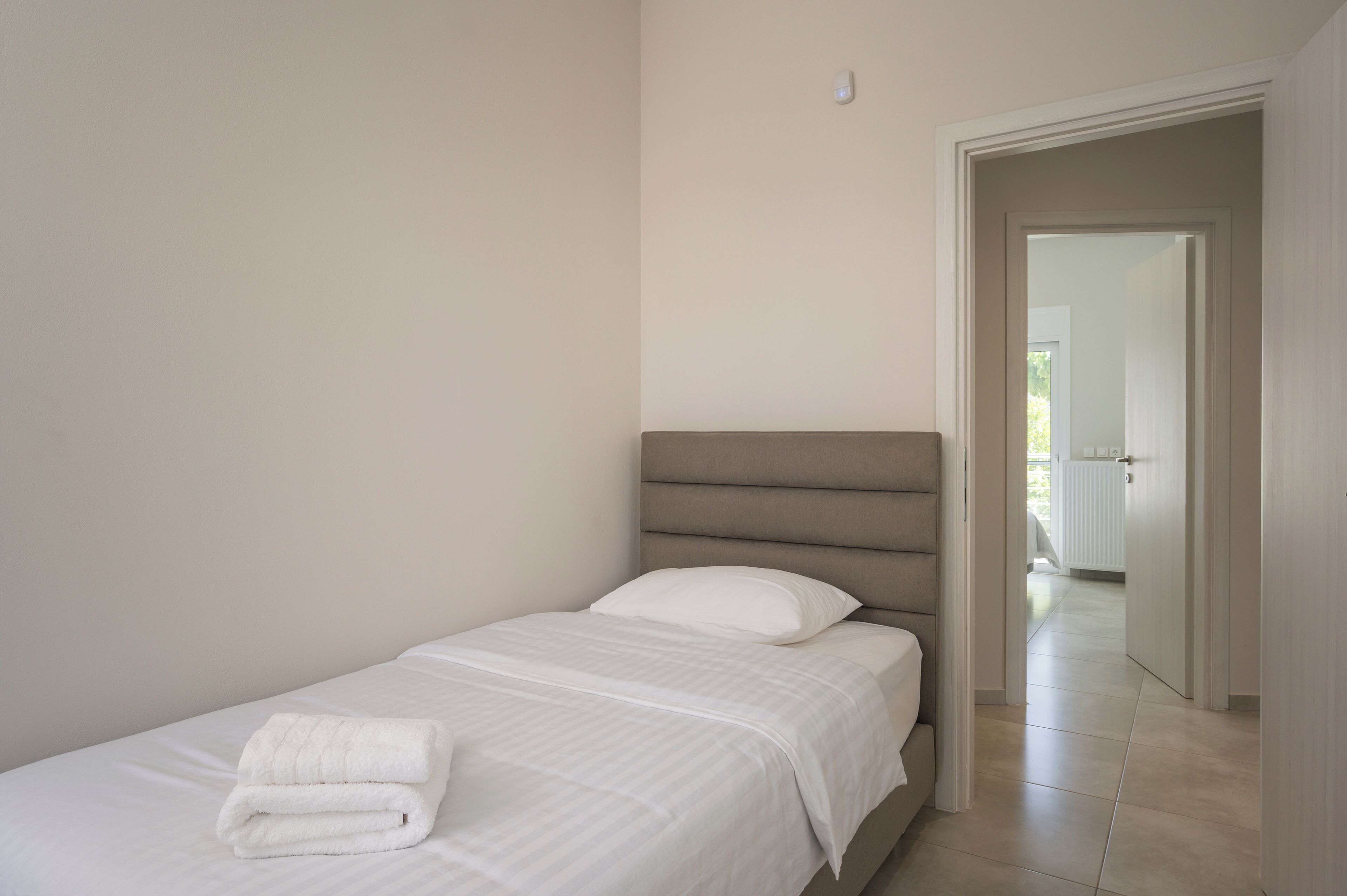 Una cama bien hecha con una toalla blanca doblada, un cabecero y una pared lisa.