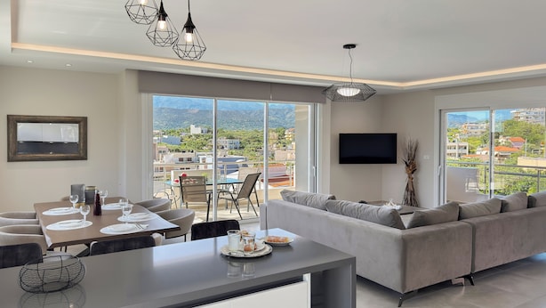 Una sala de estar moderna con comedor, ventanas grandes y un televisor de pantalla plana.