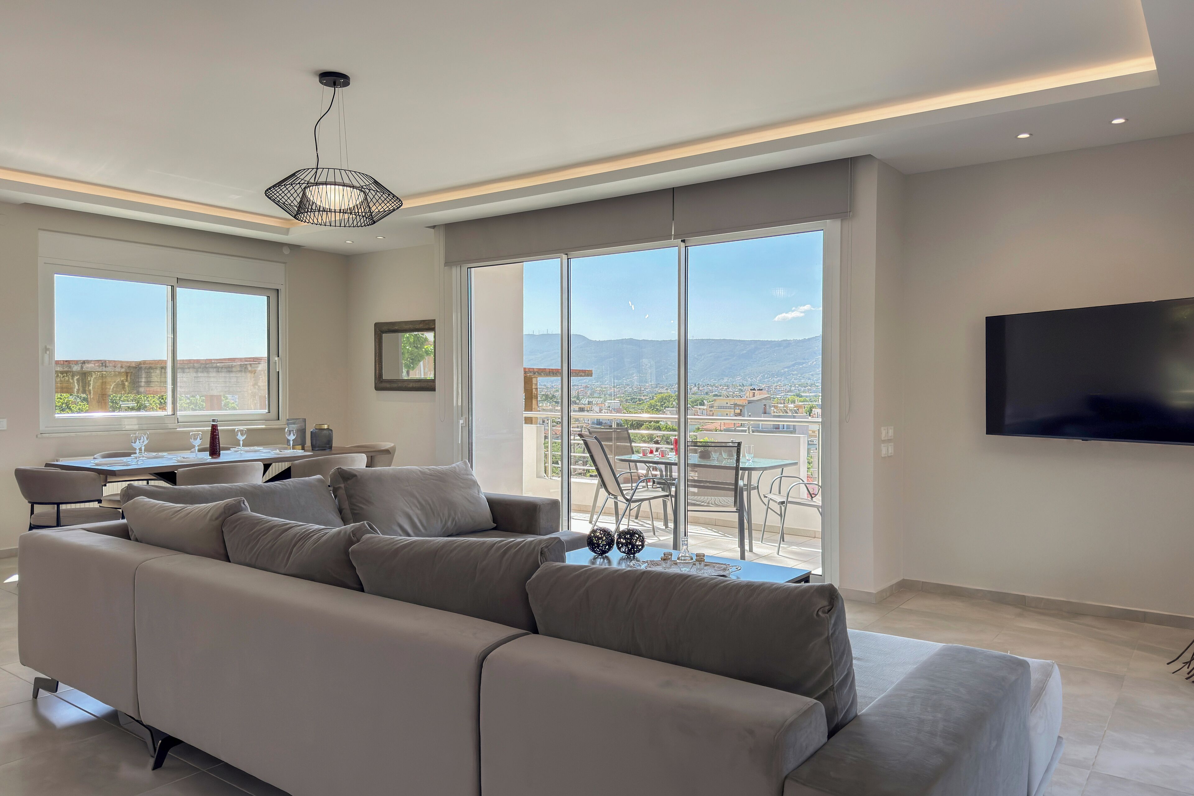Ein modernes Wohnzimmer mit einer großen Couch, einem Essbereich und einem Balkon mit Blick auf die Stadt.