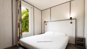Een slaapkamer met een bed, nachtkastje, raam met gordijnen en een wandlamp.