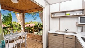 Een keuken met houten kastjes, een spoelbak en een magnetron. Er is een eethoek met stoelen en een tafel.
