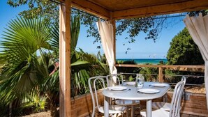 Een terras met een houten pergola, witte metalen stoelen en een tafel gedekt voor twee personen.