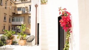 Un balcon agrémenté de plantes en pot, d’une chaise et d’une porte ornée d’une guirlande de fleurs.