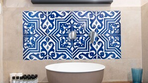 Une salle de bain avec un grand lavabo blanc, un pare-chocs en carreaux bleus et blancs, et une rangée de produits de toilette posés sur le comptoir.