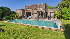 Una casa moderna con piscina, mobiliario exterior y una pérgola.