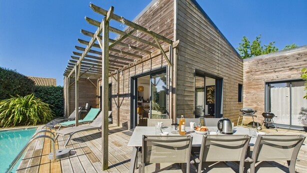 Una terraza de madera con piscina, mobiliario exterior y un pérgola.