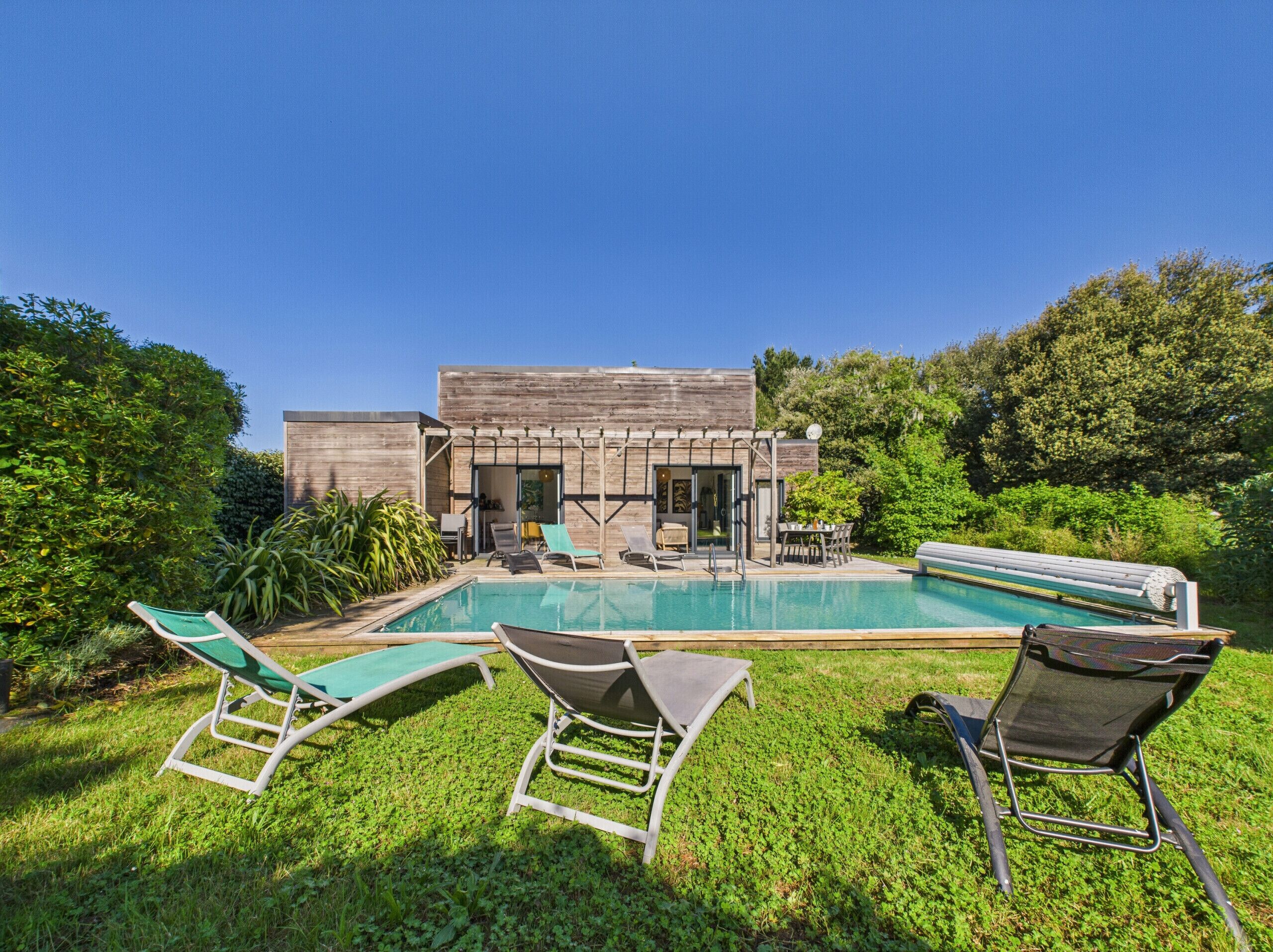 A modern house with a swimming pool, surrounded by lush greenery and equipped with outdoor furniture.
