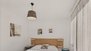Un dormitorio con cabecera de madera, cubrecama blanco, dos mesitas de noche, una lámpara colgante y decoración en la pared.