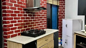 Eine kompakte Küche mit roter Backsteinwand, einer Edelstahl-Dunstabzugshaube, einem Gasherd, Holzschränken und einem weißen Kühlschrank.